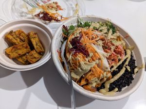 Side of corn fritters, fresh greens, black coconut rice base, sweet potato, sesame broccoli, black eyed pea tempeh, raw root vegetables, spicy slaw with coconut curry sauce. at Della Bowls in Miami