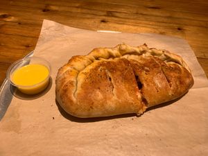 Calzone filled with red sauce, vegan cheese, mushrooms, green bell pepper, red onion and a side of vegan garlic butter at Dells Pizza Lab in Wisconsin Dells