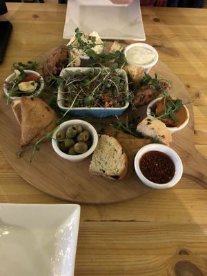 Sharing board for 2: selection of home baked breads, roasted vegetables, houmous, handmade onion bhajis and samosas, olives, Raitia yoghurt and mint dip and salad of the day. at Super Natural Newcastle in Newcastle Upon Tyne