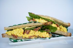 Breakfast Sandwich made from tofu scramble, vegan bacon, vegan cheese, seasonal greens, tomato, and vegan mayo on crispy toast bread at Glowing Plant Based Eatery in Los Angeles