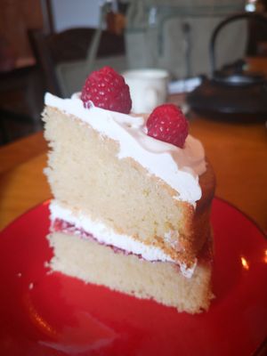 Close up of a slice of Victoria sponge cake on a red plate, sandwiched with vegan creme and jsm, topped with creme and a raspberry at Planetwise & Yoga Studio in Bridlington