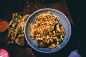 Vegan potato wedges (the crispiest, most delicious ever) smothered in herbs, cashew cheese aoli and crispy fried onions. On the side are fresh tacos with creamy avocado at Teva in Rio De Janeiro