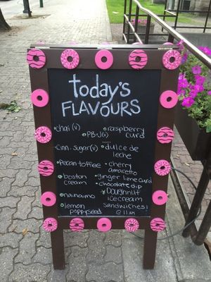 Sandwich board on street listing daily flavours (those marked "v" are the vegan options). at Oh Doughnuts in Winnipeg