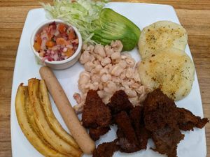 Traditional food plate: mote, marinated soy meat, pork-like sausage, fried banana, potato pancakes, salsa, and avo. at El Maple in Quito