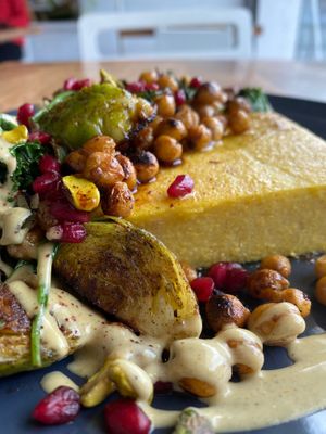 Baked polenta with Moroccan spiced roasted chick peas, Brussels sprouts, pistachios, pomegranate, leafy greens, tahini orange sauce. at The Little Shop of Plenty in Maylands