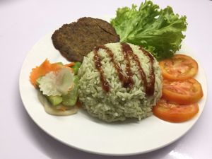 Mock beef cutlet with vegetable side salad, tomatoes and green herbs rice.  at Sweet Root Vegetarian Restaurant  in Phnom Penh