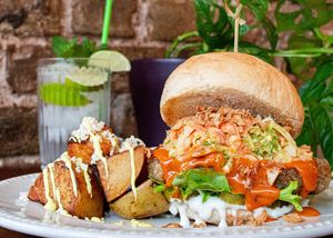 BUFFALO CHICK’N BURGER: crispy chick’n, house buffalo hot sauce, slaw, gherkin, mayo, lettuce, crispy onions. Roasted potatoes with cheez, garlic aioli.
 at Miranda Cafe in North London