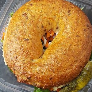 Hendricksons whole grain or sesame bagel sandwich with house lemon basil hummus and layer cucumbers, tomatoes, shredded carrot, home made peppercorn vegan mayo, mustard and a pickle.  at Frickin' Delights Donuts in Devon