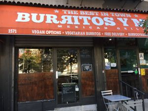 Outside entrance, with simple outdoor seating: notice Happy Cow sticker on front door! at Burritos y Mas in New York City