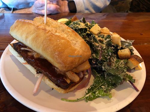 Korean Brisket Sandwich with Kale Caesar Salad. Slow cooked BBQ tempeh brisket, pickled onions, bread and butter pickles, kimchi, and cabbage slaw on a rustic baguette. at Bad Apple  in Vancouver