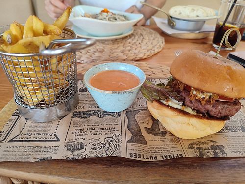 Hamburguesa vegana de beyond burguer. Es de pequeño tamaño pero está muy buena. Lleva lechuga, tomate, cebolla crujiente y una salsa. Las patatas llevan una salsa picante. Segú at Cala Petita in Mallorca