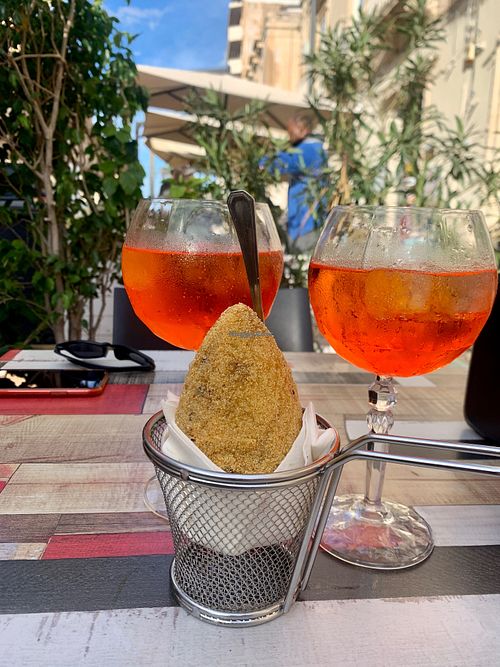 Anne enjoying an Aperol spritz, arancini pairing at Vegan Food Tour Ortigia in Siracusa