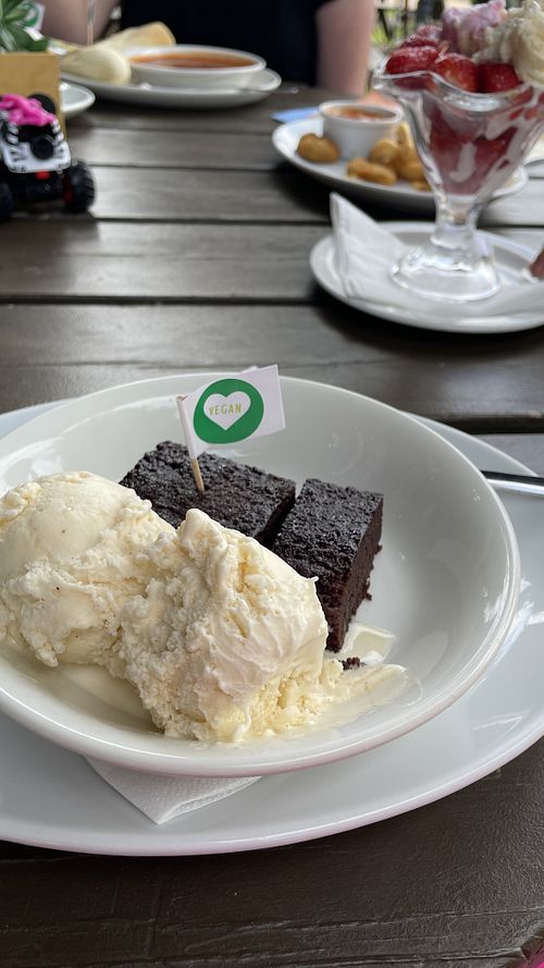 Warm brownie with ice cream. In the background is: tomato soup with baguette and vegan spread; “chicken” nuggets, chips and baked beans; and strawberries and ice cream.  at Old World Tea Rooms in Ventnor