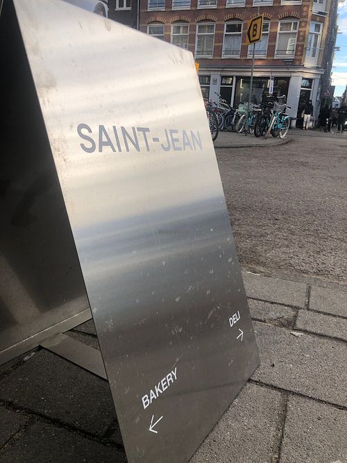 The shiny sign across the street pointig to the deli on the corner in the distance. at Saint-Jean Deli in Amsterdam