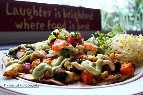 Roasted Veggie Tostada with seasoned, roasted, organic veggies on a toasted 7-grain & flax tortilla with a melty blend of cheddar, pepper jack, and mozzarella cheeses, topped with tasty veggie pico de gallo, chipotle aioli, and creamy avocado drizzle at Sprouts Cafe in Gastonia
