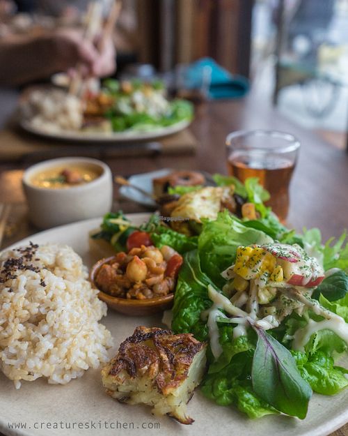 Vegan lunch plate set with brown rice, salad, miniature okonomiyaki, veggie mince meat, stir-fried vegetables, daikon with komatsuna and yuzu, carrot soup, cake, and tea.  at Komeday in Osaka