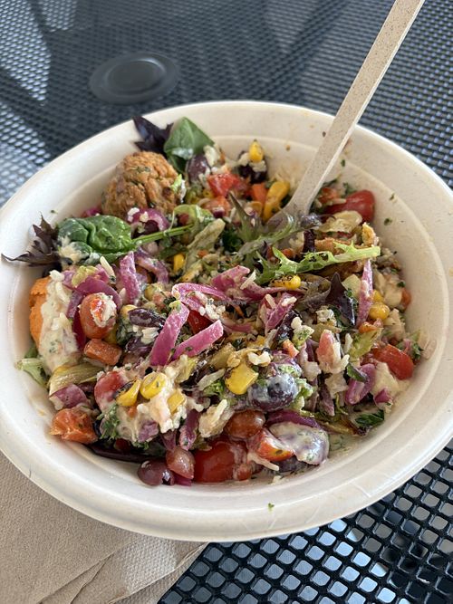 Bowl with base of brown rice and greens, half falafel an half roasted veggies, hummus, eggplant, corn, picketed onions, tomatoes, olives, and vegan lemon tahini dressing   at CAVA - Long Beach in Long Beach