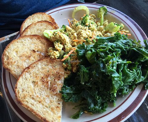 Breakfast scramble served w/ garlic-steamed greens & brown rice toast, seasoned tofu, green peppers, onions, mushrooms, broccoli, & carrots. Vegan cheese blended into seasoned tofu, scrambled w/green peppers onions, & mushrooms topped w/tomatoes. at The Wayward Vegan in Seattle
