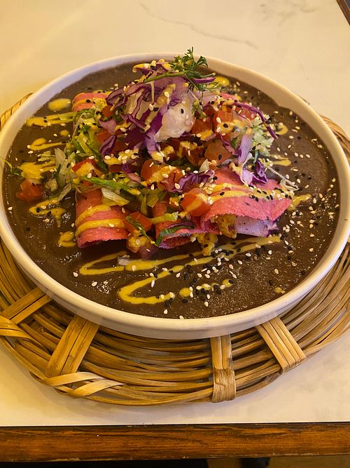 Enfrijoladas - frijoles negros cremosos sobre tortillas rosas rellenas de plátanos, almendras crocantes, requesón de coco fresco, y pico de gallo. at La Pitahaya Vegana in Mexico City