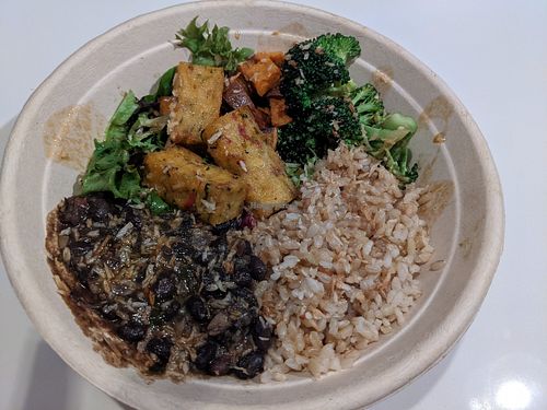 Brown ride fresh greens base, sweet potato, sesame broccoli, black beans sofrito, toasted coconut, corn fritters with ginger tamari gold sauce at Della Bowls in Miami