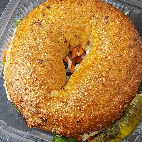 Hendricksons whole grain or sesame bagel sandwich with house lemon basil hummus and layer cucumbers, tomatoes, shredded carrot, home made peppercorn vegan mayo, mustard and a pickle.  at Frickin' Delights Donuts in Devon